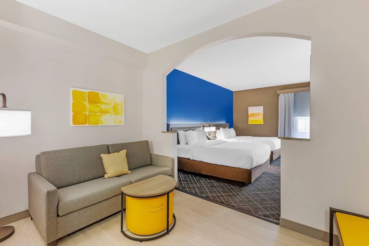 A hotel room with a bed, a sofa, a small table, and artwork on the walls.