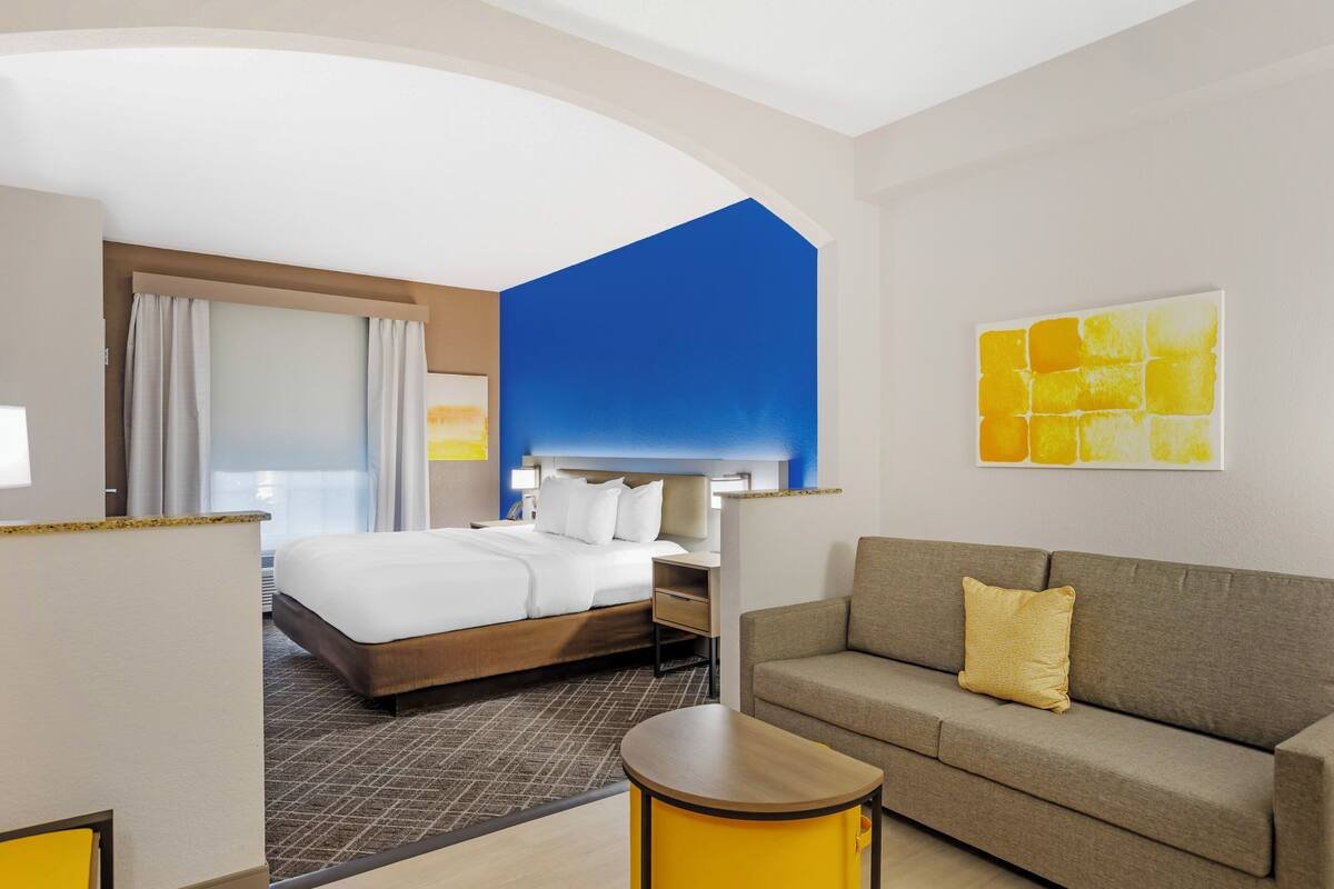A hotel room with a bed, a sofa, a round table, and a painting on the wall.