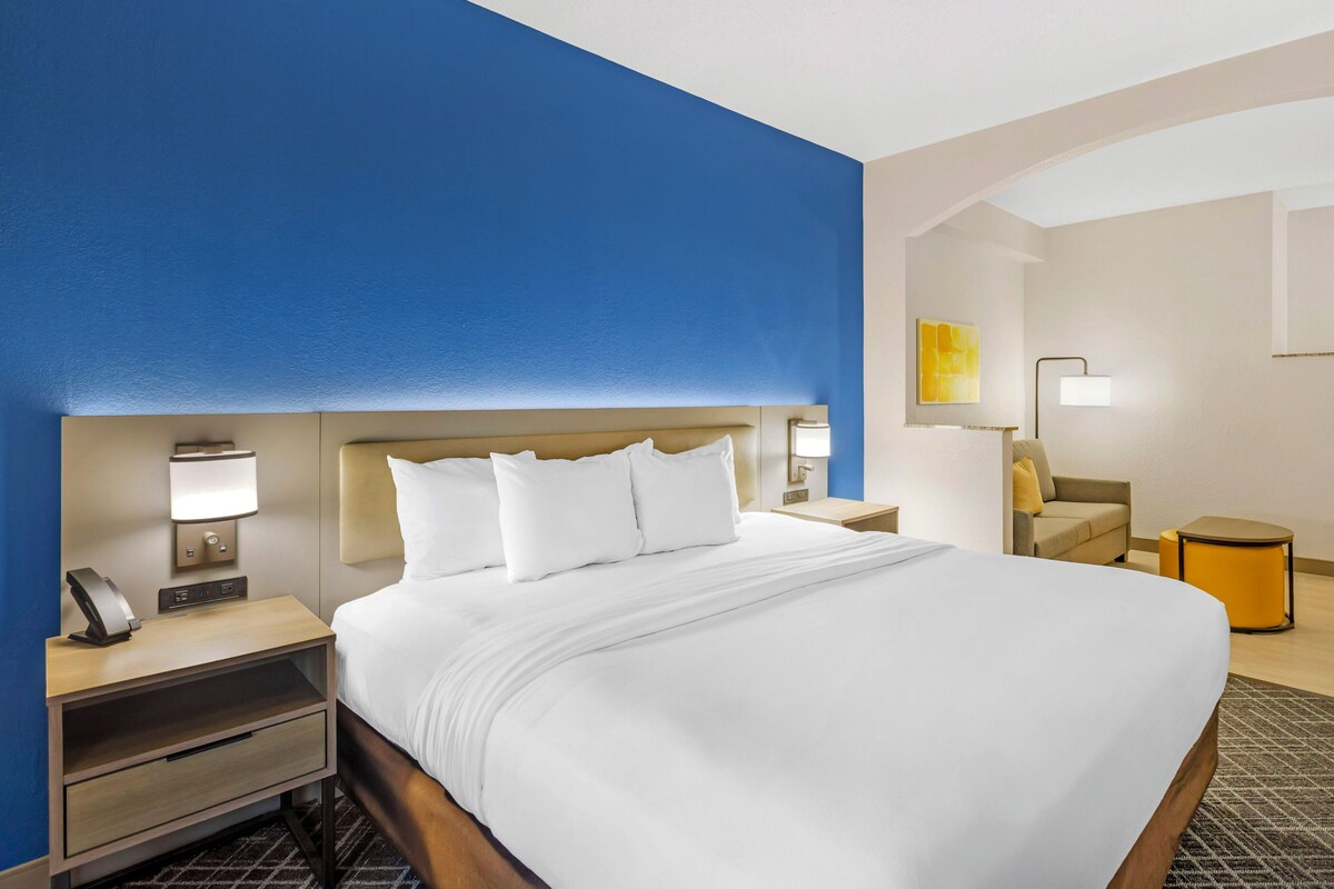 Habitación de hotel con una cama grande, mesitas de noche, una lámpara, una silla y una pequeña mesa.