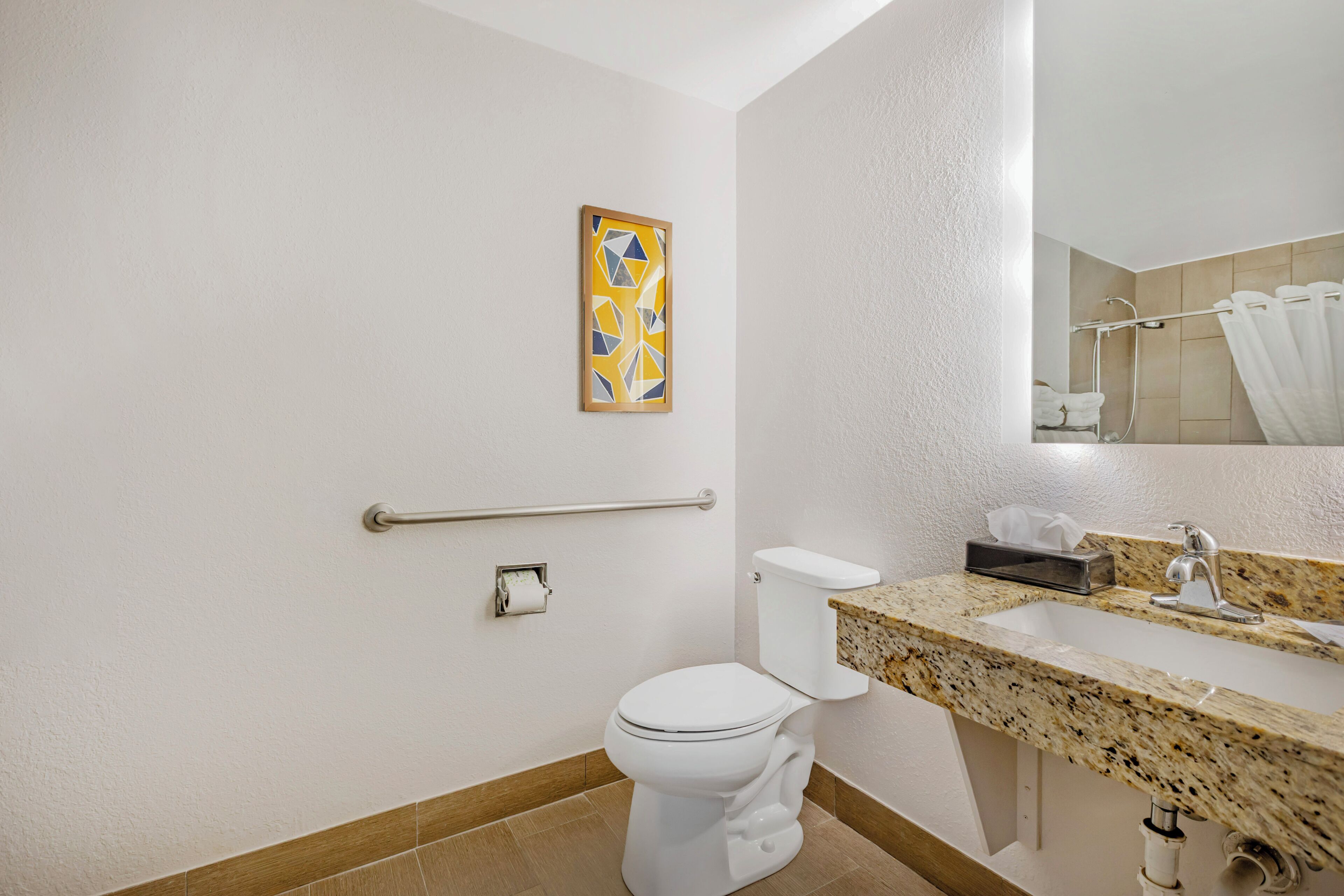 Un baño con inodoro, lavamanos, espejo, toallero y barra de apoyo.