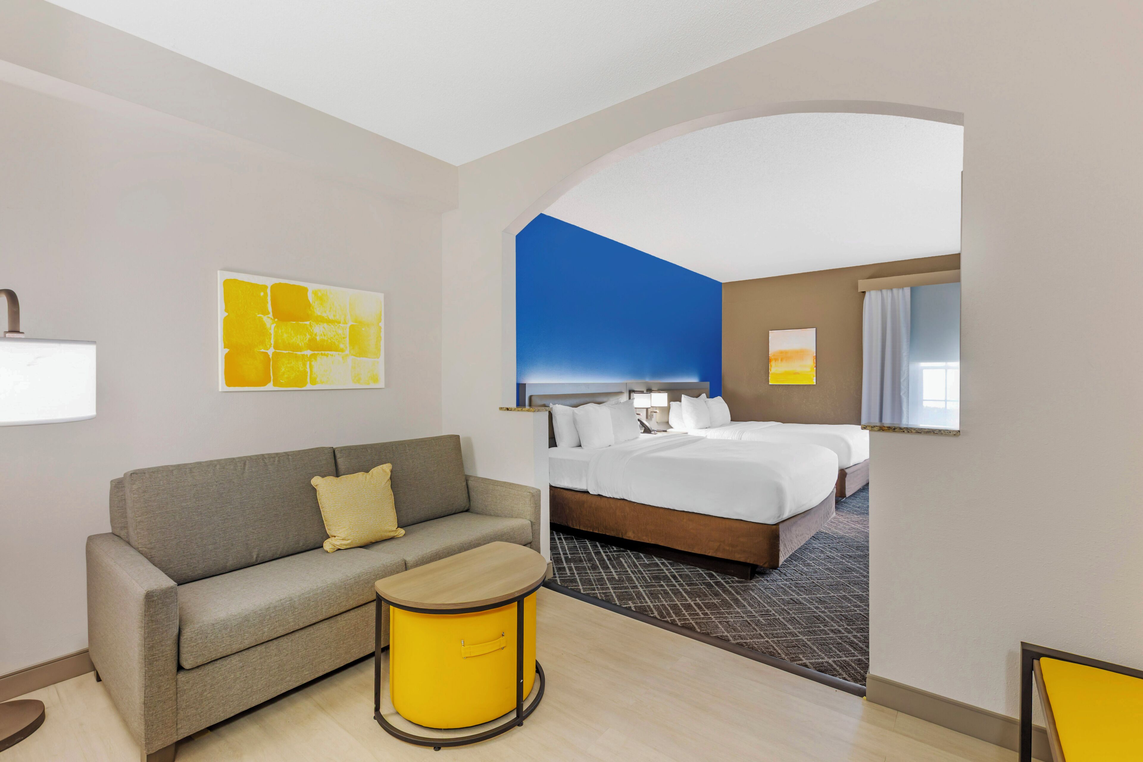 Une chambre d’hôtel avec un lit, un canapé, une petite table et des œuvres d’art accrochées aux murs.