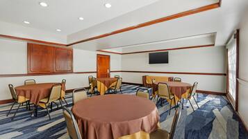 A conference room with round tables, chairs, a flat-screen TV, and a large window.