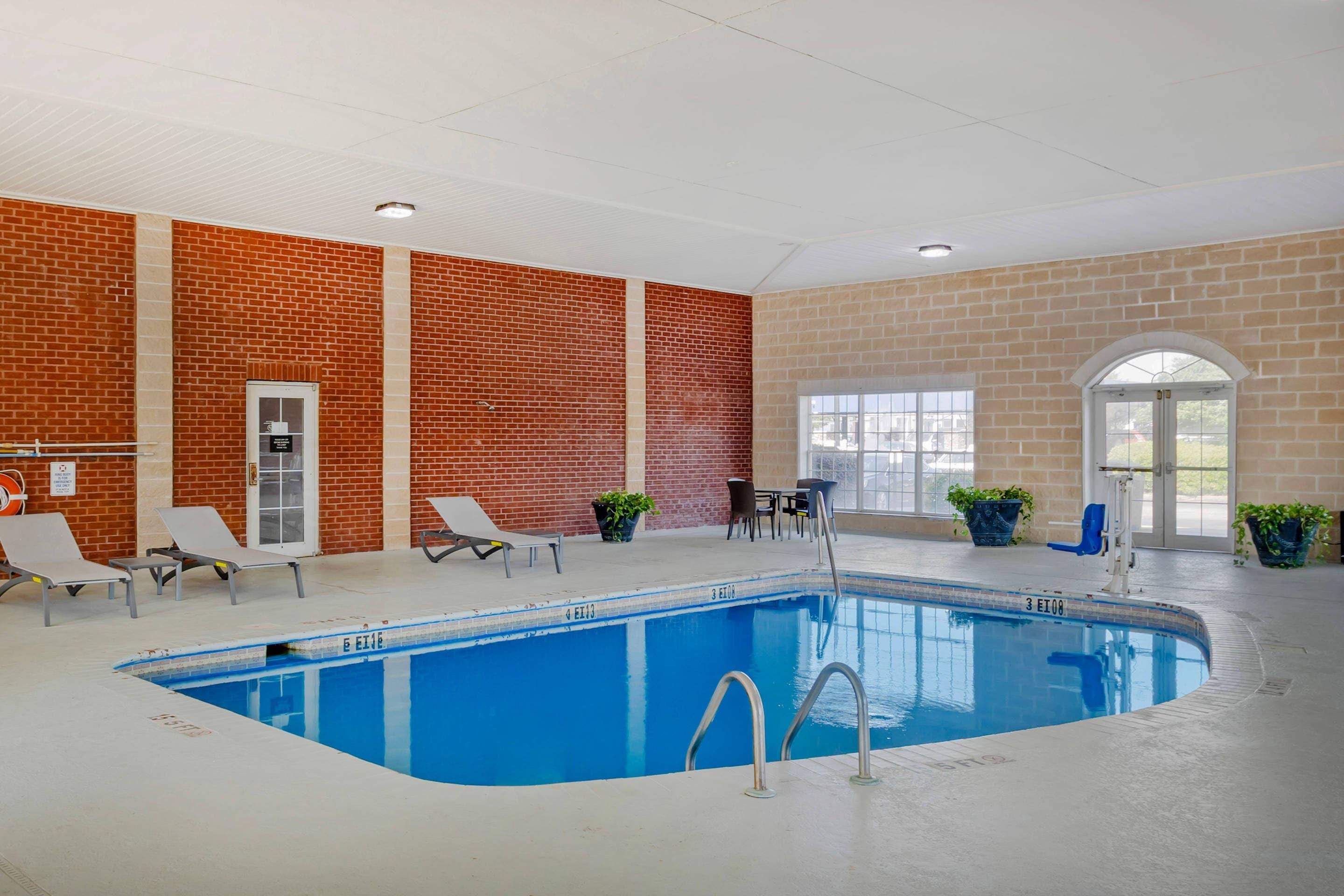 An indoor swimming pool with lounge chairs, a table, and potted plants.