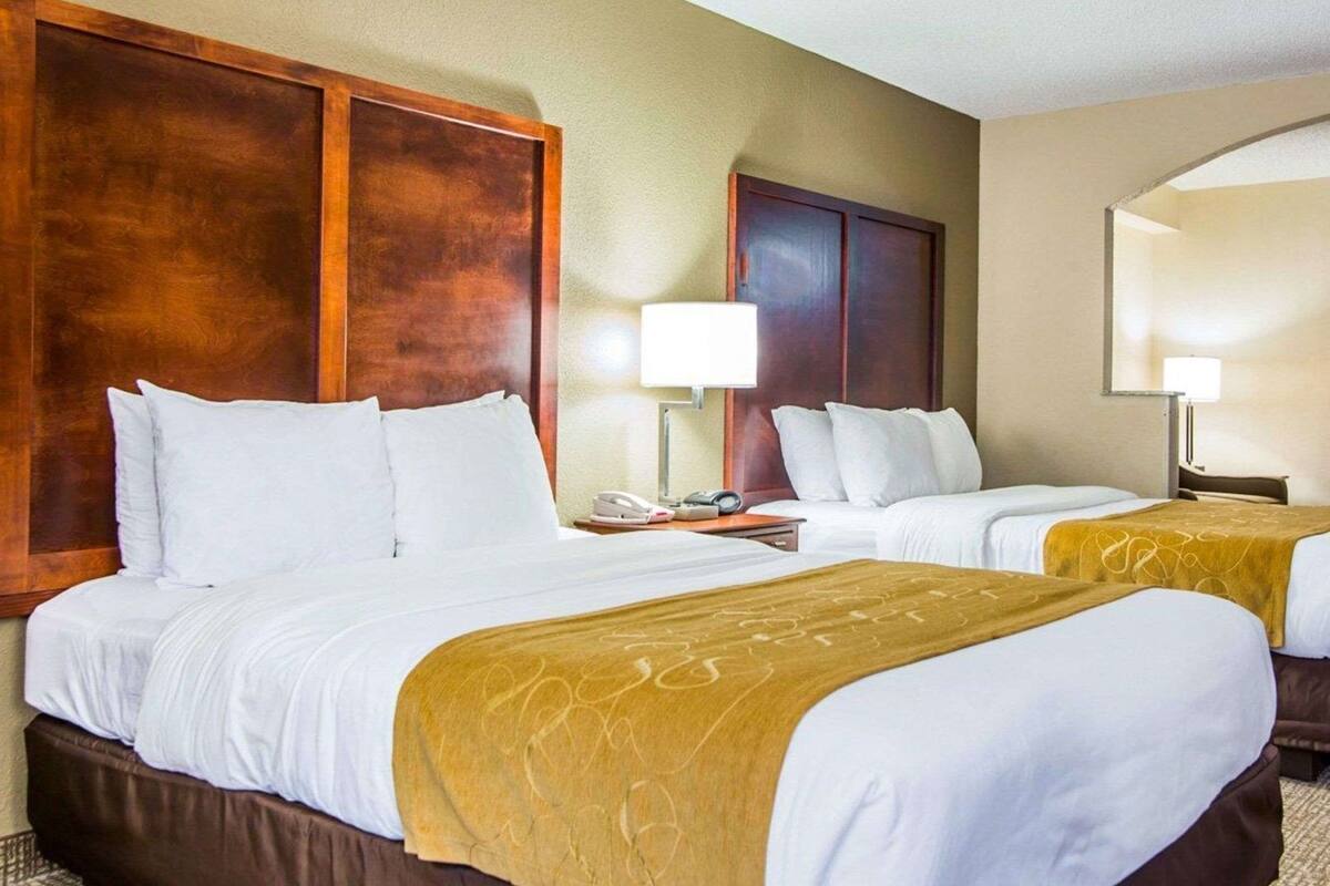 A hotel room with two beds, a wooden headboard, a nightstand with a lamp, and a telephone.