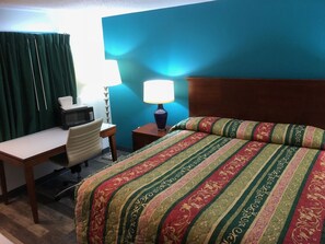 A hotel room with a bed, desk, chair, and a lamp.