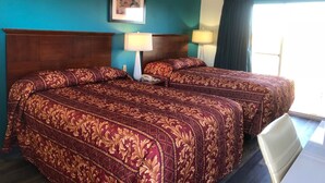 Habitación de hotel con dos camas, cada una con colcha estampada, cabecero de madera, lámpara de noche e imagen enmarcada en la pared.