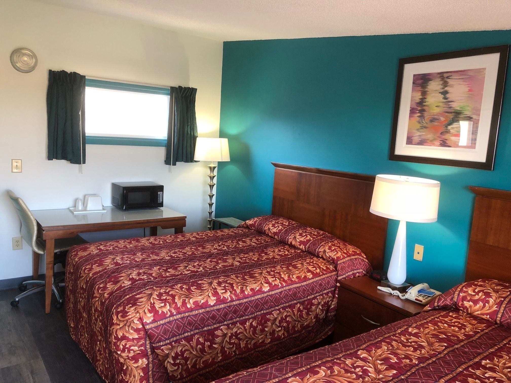 Een hotelkamer met twee bedden, een bureau, een magnetron, een telefoon en een schilderij aan de muur.