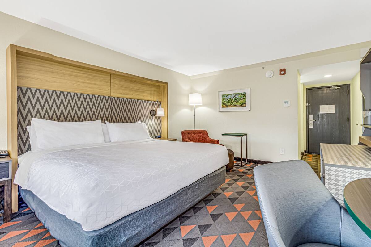 Una camera d'albergo con un letto grande, un tavolino, una sedia e una panca.