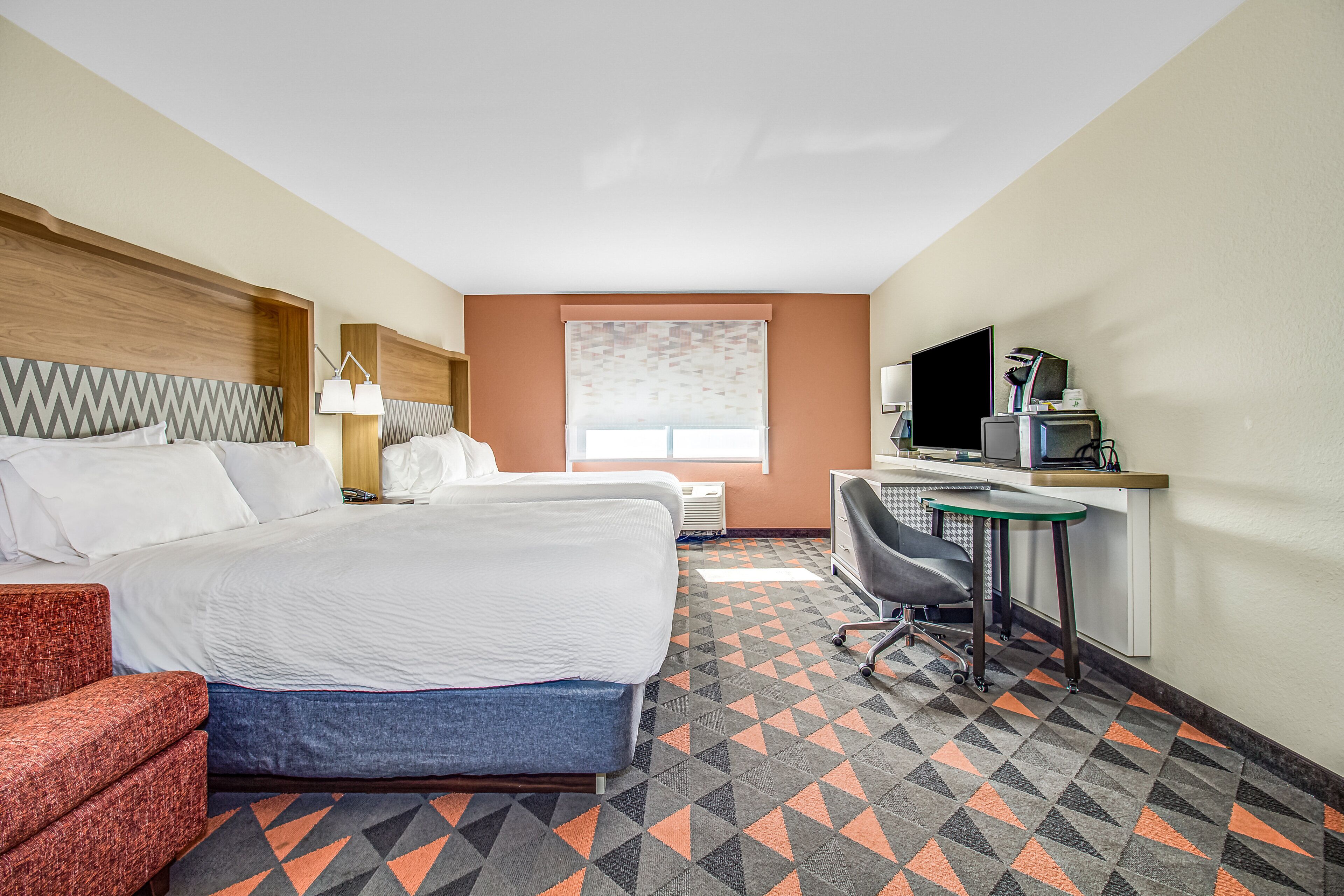 A hotel room with a bed, desk, chair, and a TV.