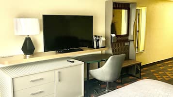 A hotel room with a bed, a desk with a television, a chair, a dresser, and a mirror.