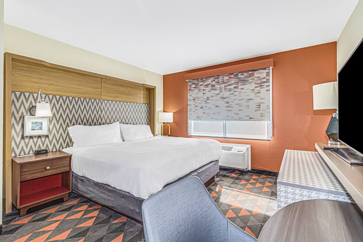 Camera d'albergo con un letto, comodino, lampada, televisore e tappeto a motivi.