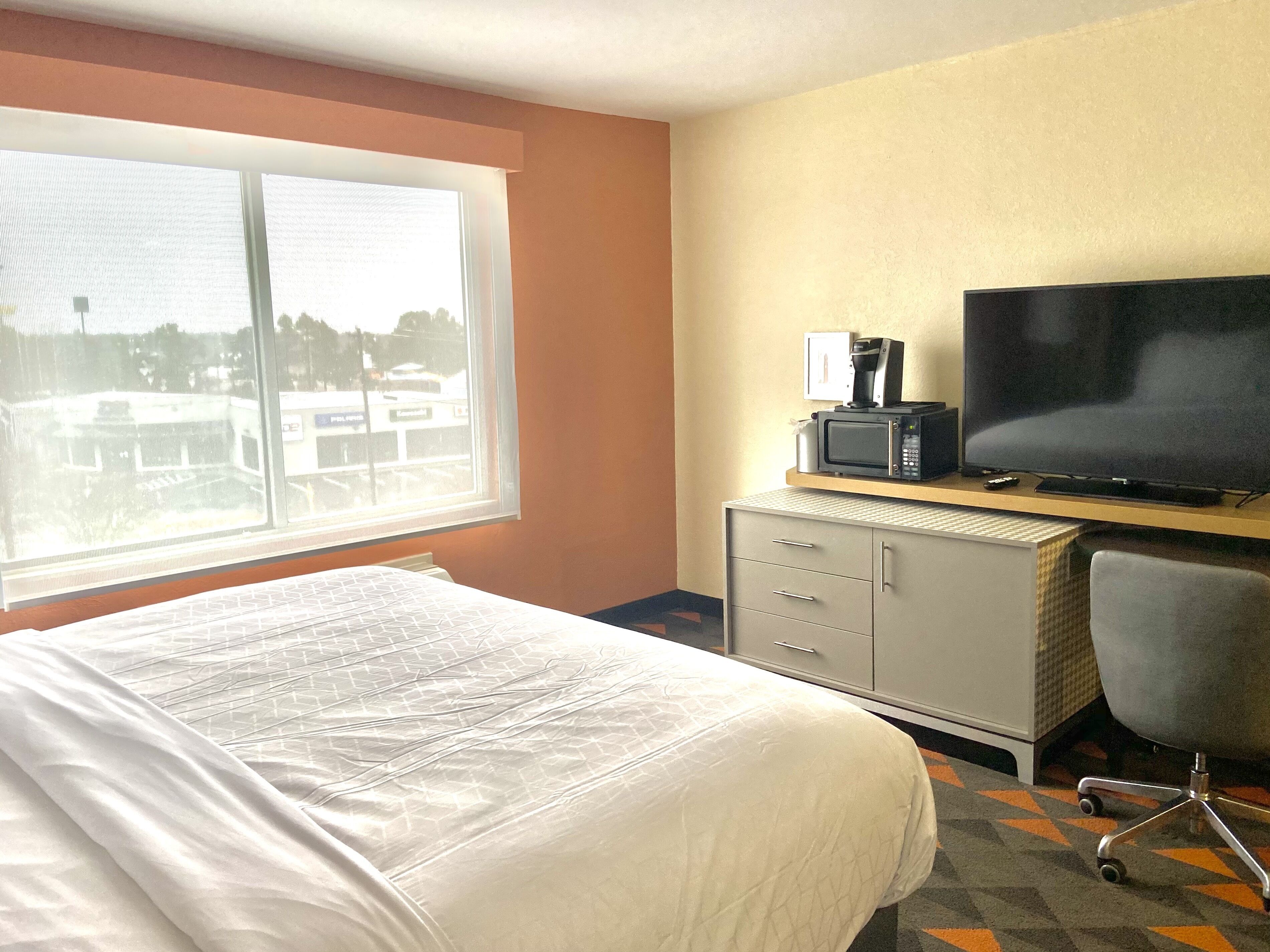 Habitación de hotel con cama, escritorio con televisor, cafetera y vista a un edificio.