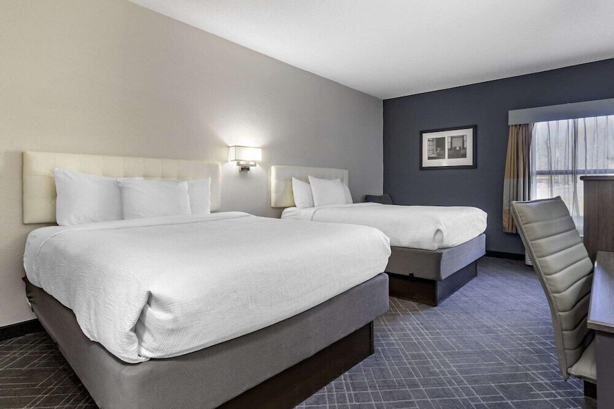 Ein Hotelzimmer mit zwei Betten, einem Schreibtisch, einem Stuhl, einem Fenster und einem Bild an der Wand.