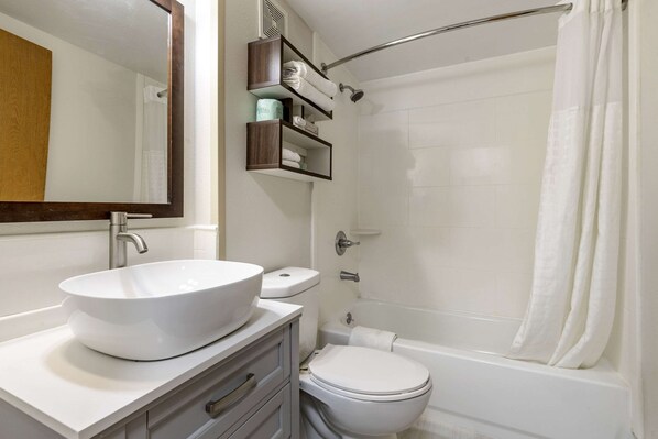 A bathroom with a white sink, toilet, and bathtub. There are shelves above the toilet holding toiletries.