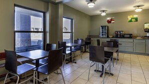 Uma cafeteria com várias mesas e cadeiras, um micro-ondas e uma geladeira.
