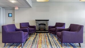 Um quarto com quatro poltronas roxas, uma lareira de pedra e um tapete listrado e colorido.