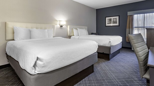 Quarto de hotel com duas camas, uma mesa e uma cadeira.
