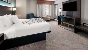 Une chambre d’hôtel avec un grand lit, un bureau avec une chaise, une télévision et une fenêtre avec des rideaux.
