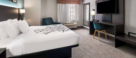 Habitación de hotel con una cama grande, un escritorio con silla, televisión y ventana con cortinas.