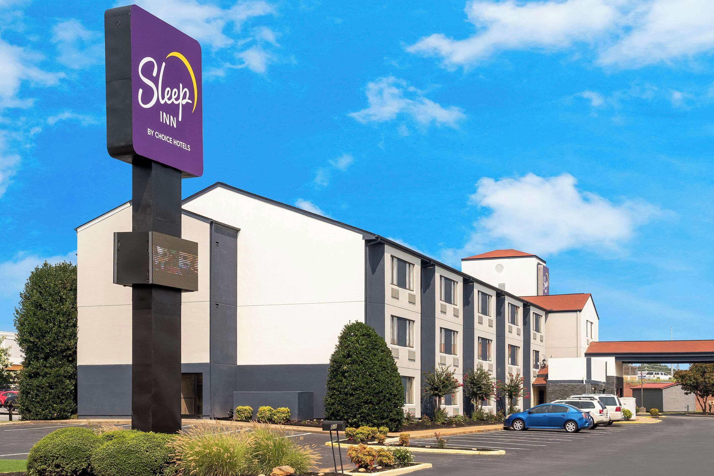 A Sleep Inn by Choice Hotels building with a parking lot and a blue car parked in front.