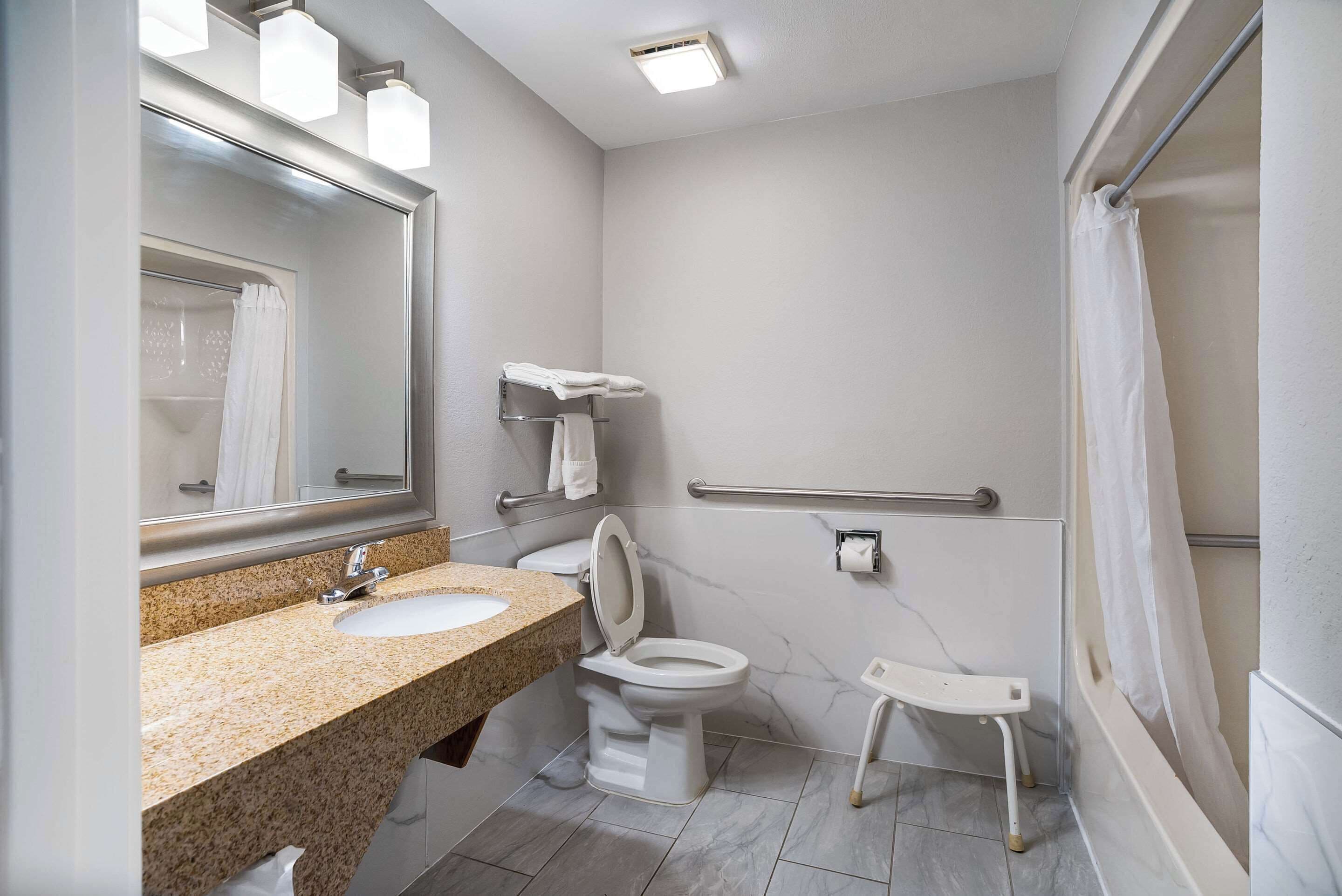 A bathroom with a granite countertop sink, a white toilet, a mirror, and a shower with a glass door.