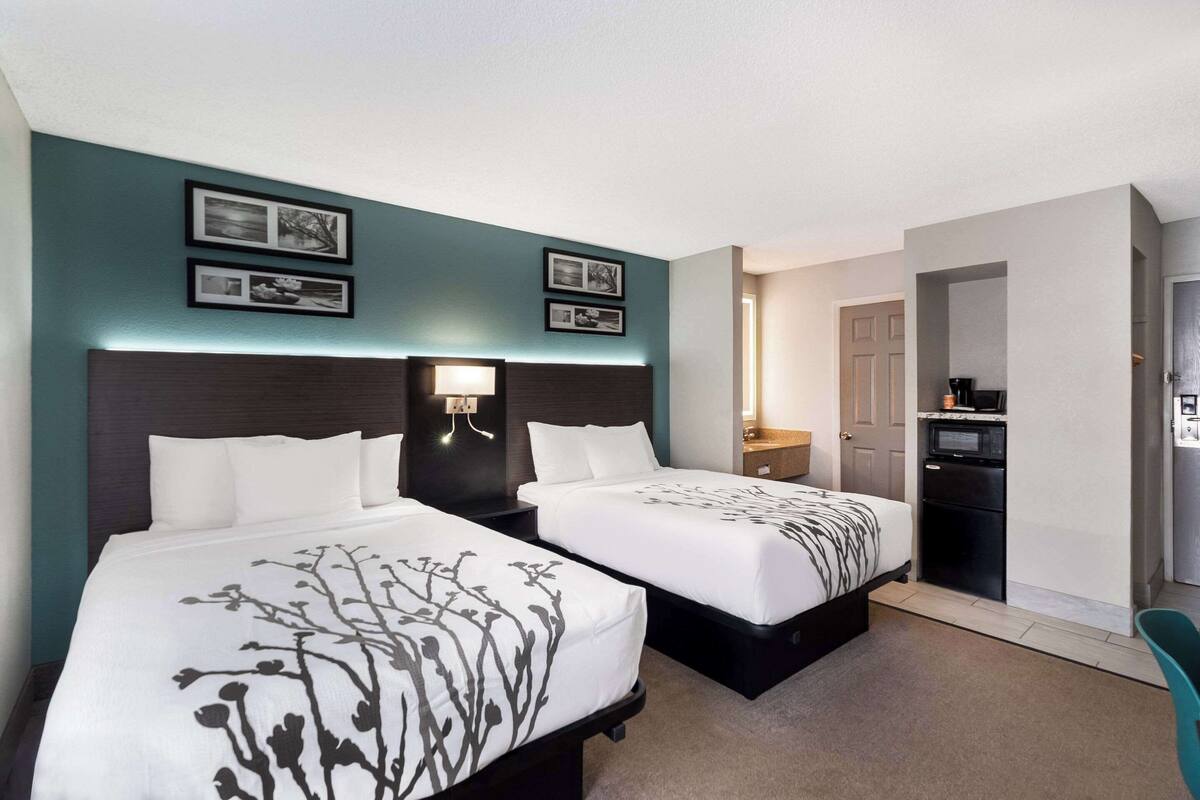 A hotel room with two beds, a desk, a microwave, and a door leading to another room.