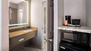 Une salle de bain avec un lavabo doté d’un plan de travail en granit, un grand miroir, un four à micro-ondes et une machine à café.