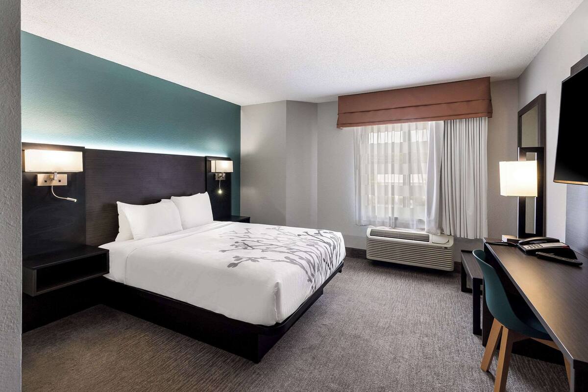 A hotel room with a bed, bedside tables, a desk, and a TV.