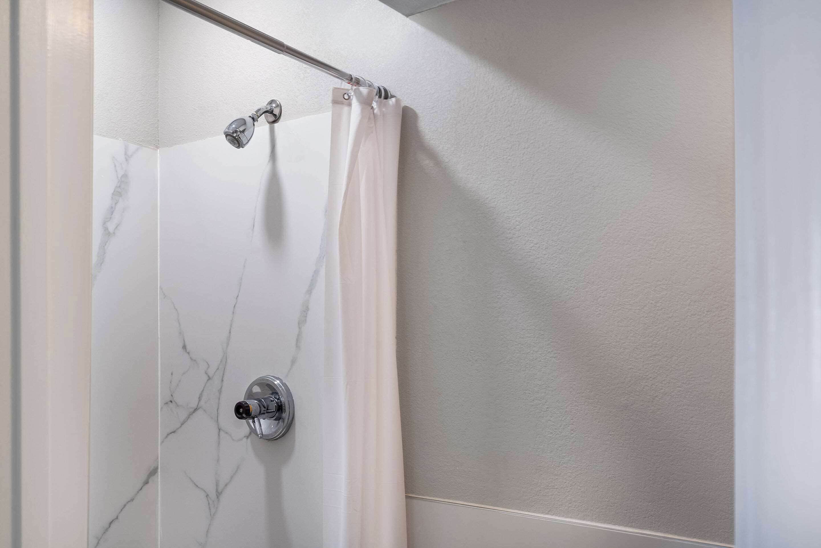 A shower with a marble wall, a showerhead, and a curtain.