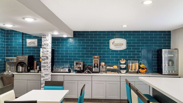 Un espace moderne dédié au petit-déjeuner, avec un mur recouvert de carreaux bleus, un coin café et des sièges agrémentés de coussins turquoise.