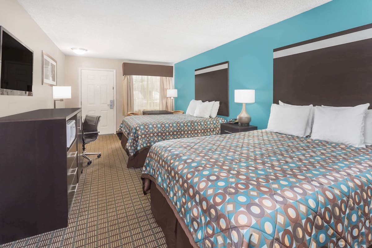 A hotel room with two beds, a desk, a chair, and a TV.