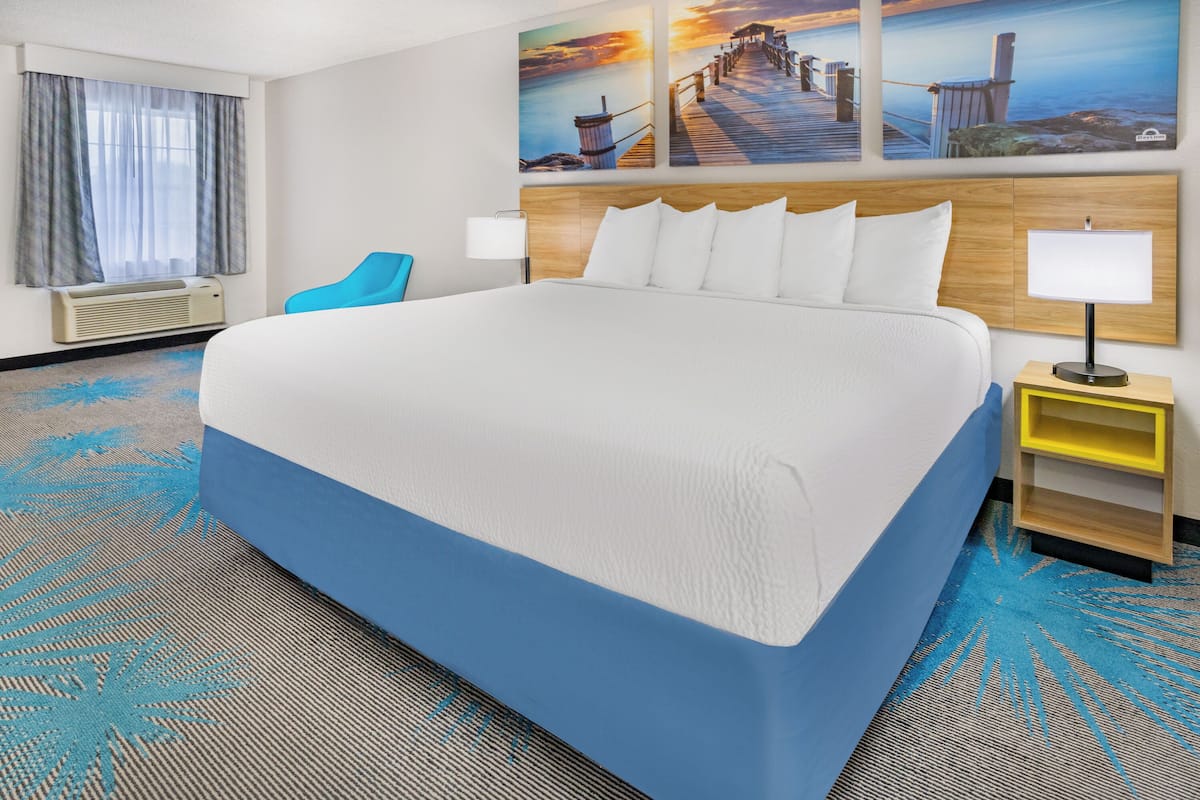 A large bed with white and blue bedding, a wooden headboard, and a nightstand with a lamp.