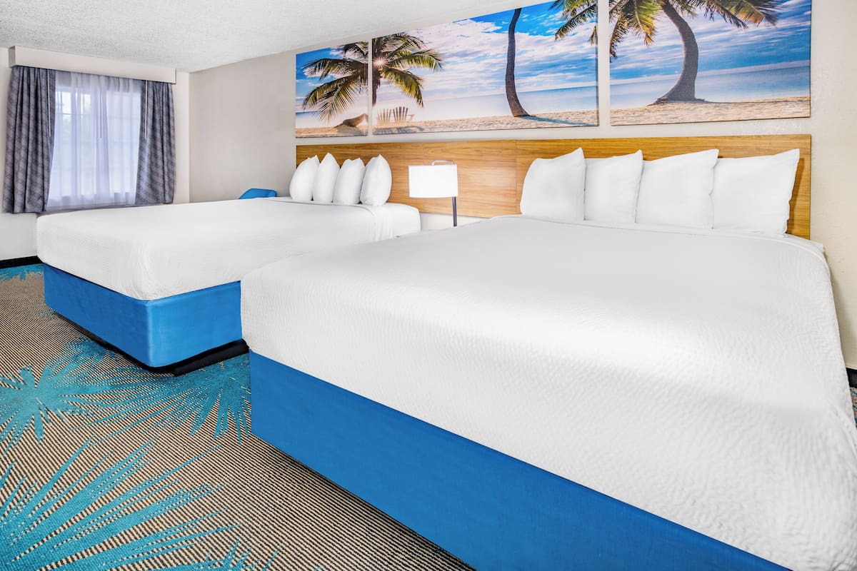 A hotel room with two beds, a large beach-themed painting, and a blue carpet.
