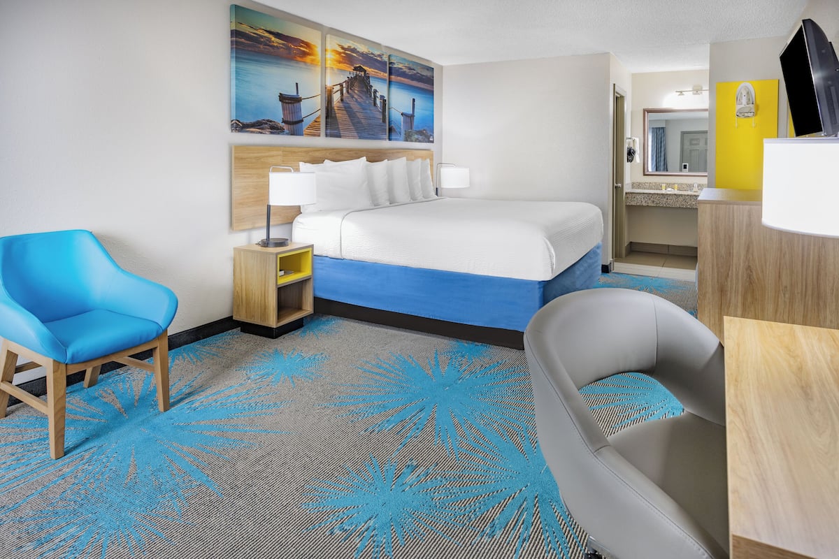 A hotel room with a bed, a desk, a chair, a bathroom, and a painting of a pier.