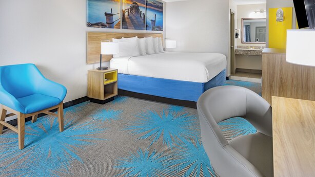 A hotel room with a bed, a desk, a chair, a bathroom, and a painting of a pier.