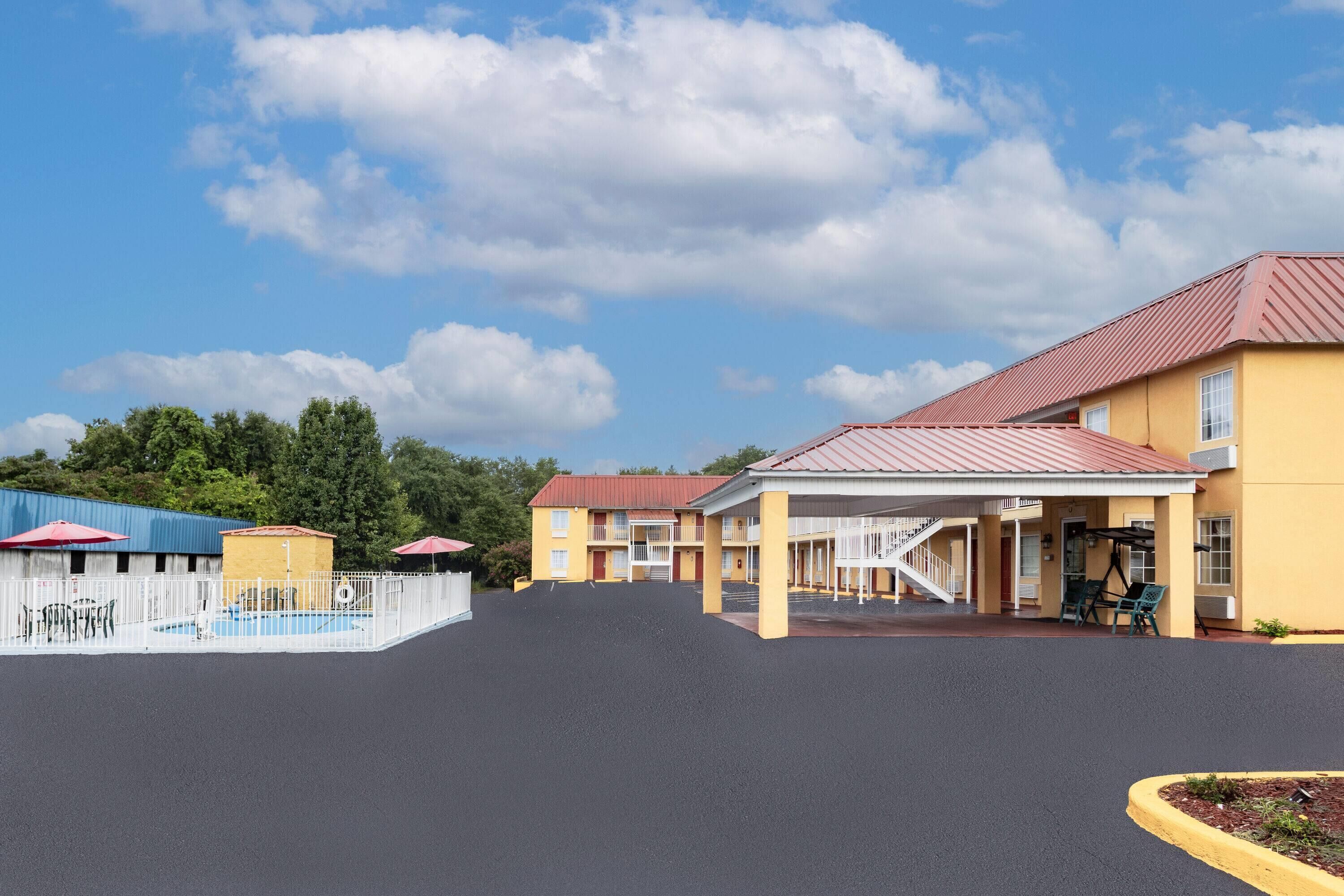 A motel with a pool, outdoor seating, and a covered area with stairs.