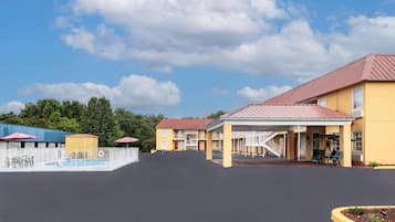 A motel with a pool, outdoor seating, and a covered area with stairs.