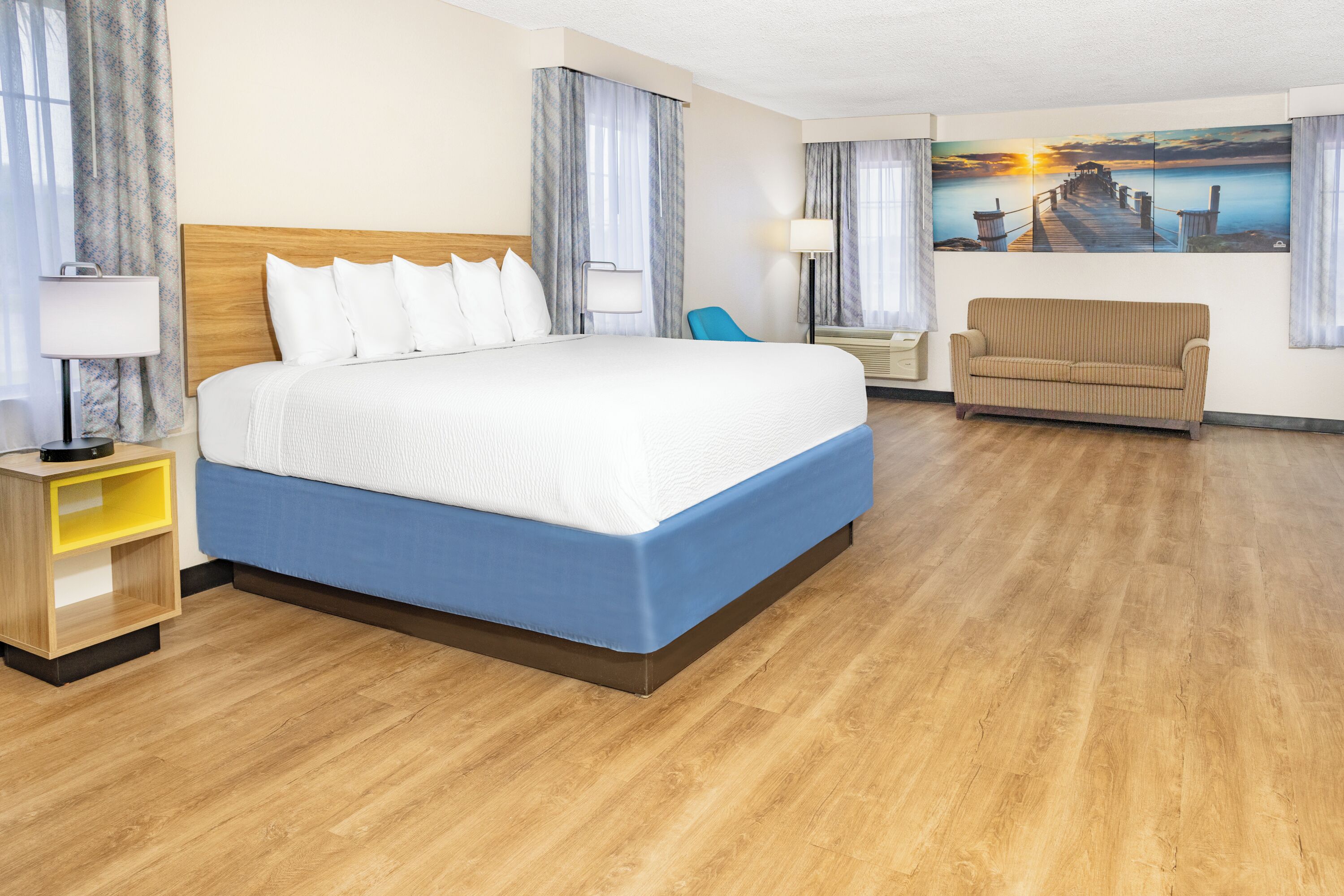 Habitación de hotel con una cama grande, un sofá, un escritorio con lámpara y un cuadro en la pared.