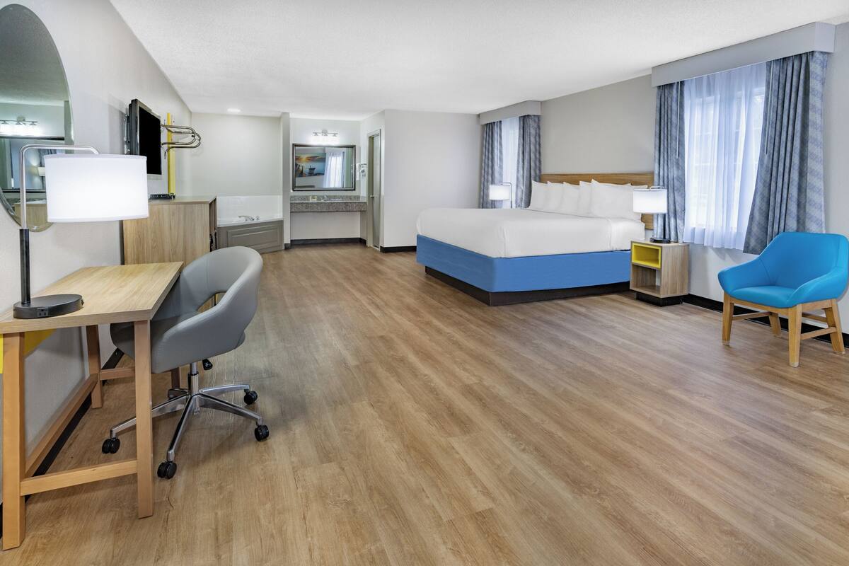 A hotel room with a bed, desk, chair, and a small bathroom area.
