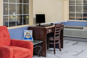 A hotel room with a wooden desk, a computer, a chair, a red armchair, and a sign on the wall. - Days Inn by Wyndham Barnwell (Barnwell)