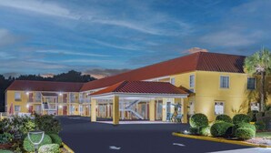 A two-story motel with a red roof and yellow exterior walls, featuring a covered parking area and a landscaped garden.