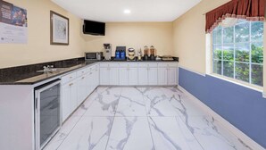 A kitchen with white cabinets, a marble floor, and a window with a view of greenery.