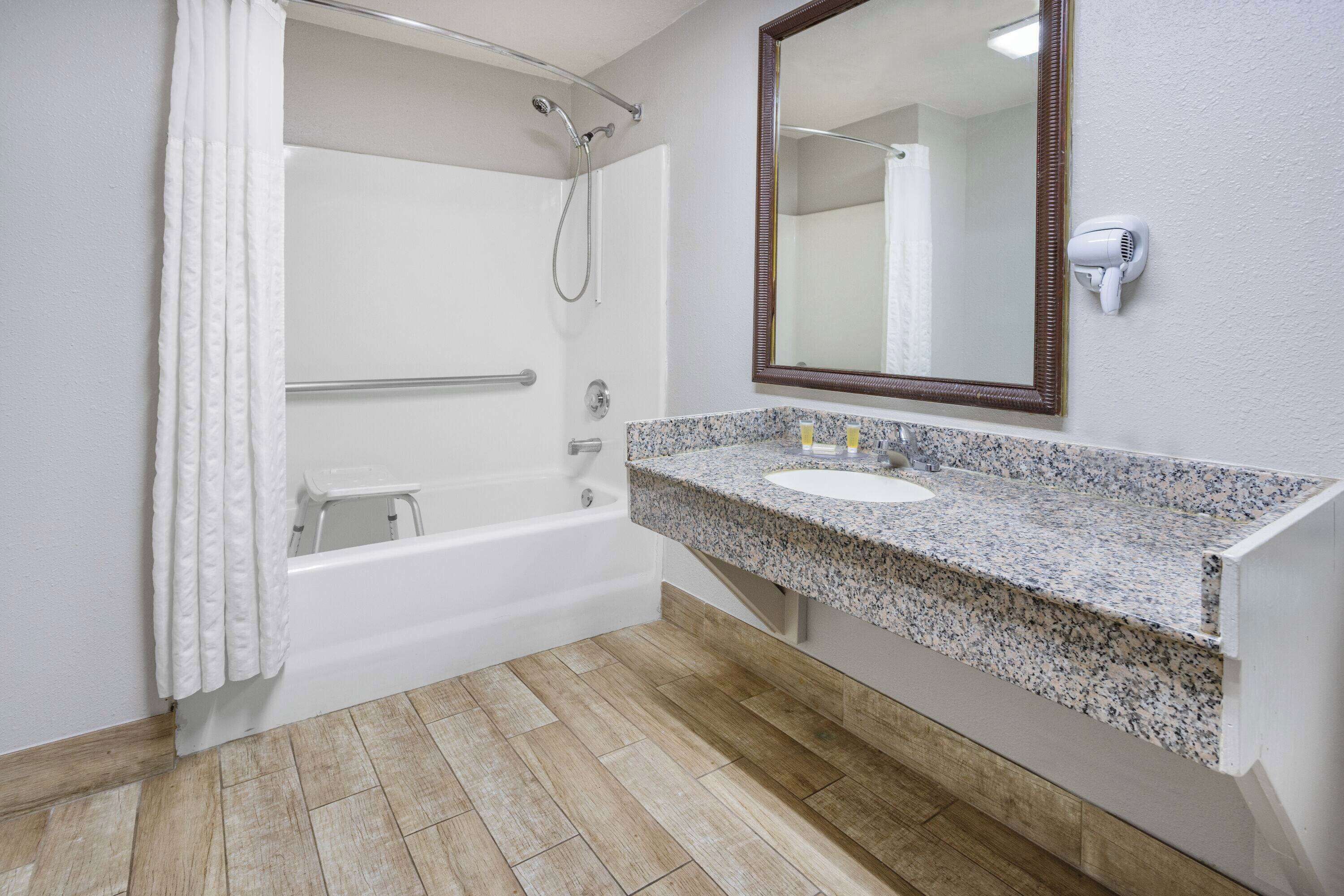 A bathroom with a white bathtub, a granite countertop sink, a large mirror, and a handheld hair dryer mounted on the wall.