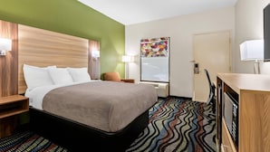 Habitación de hotel con cama, escritorio, silla, lámpara, ventana y puerta.