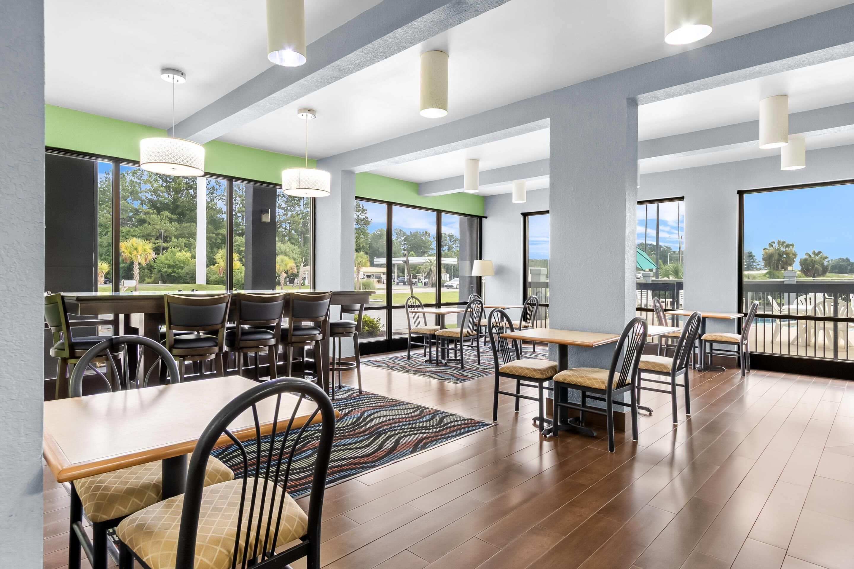 Un vaste espace intérieur aménagé pour les repas, avec de nombreuses tables et chaises, de grandes fenêtres offrant une vue sur l’extérieur et un design moderne au niveau du plafond.