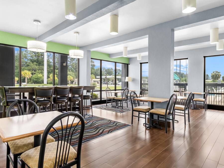 A spacious indoor dining area with multiple tables and chairs, large windows offering views of the outdoors, and a modern ceiling design.