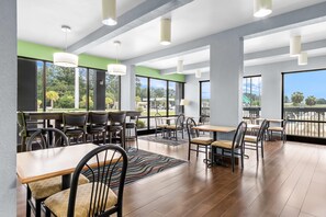 A spacious indoor dining area with multiple tables and chairs, large windows offering views of the outdoors, and a modern ceiling design.
