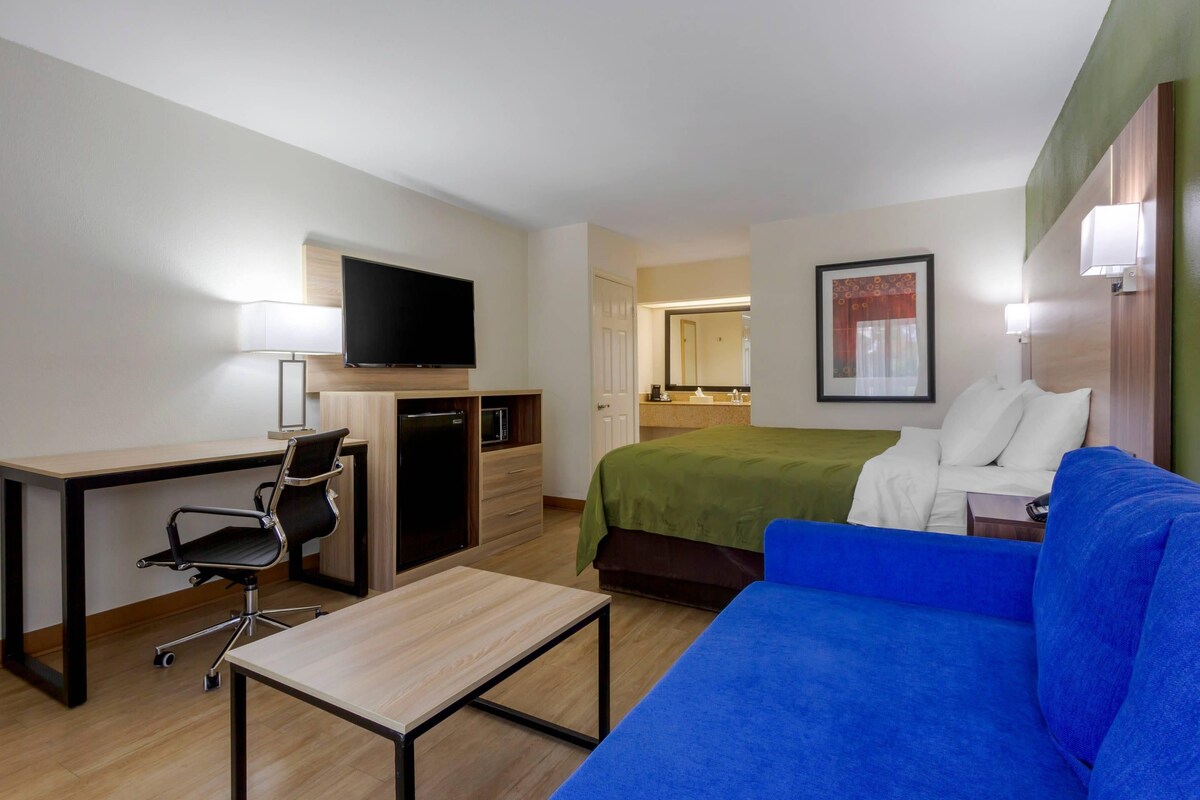Una habitación de hotel con cama, escritorio con silla, televisor, microondas y una mesita.