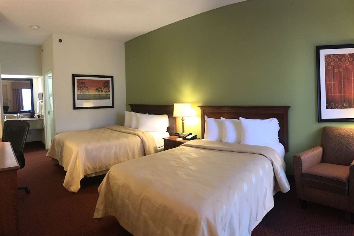 A hotel room with two beds, a chair, a desk, and a painting on the wall.