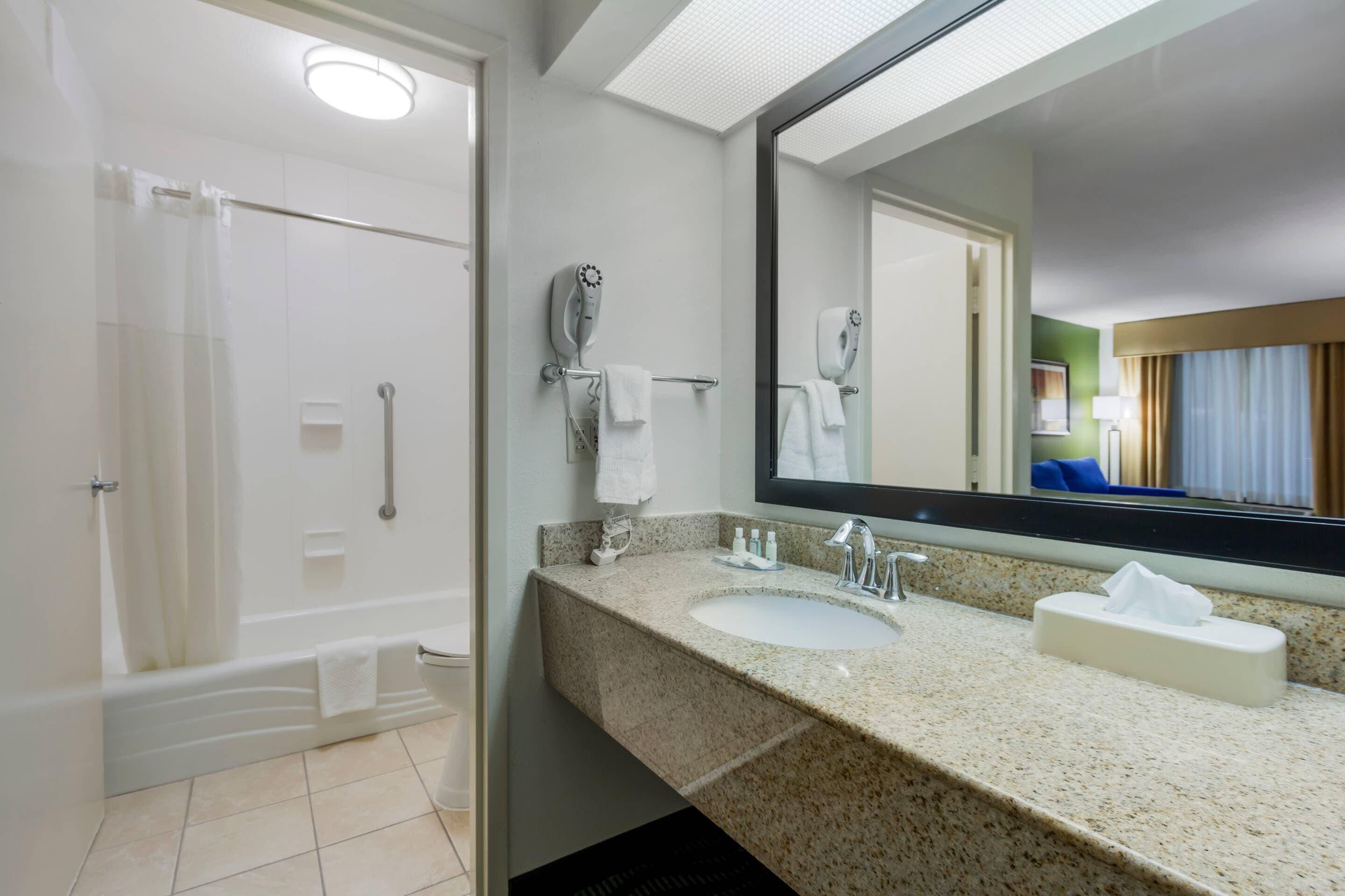 Une salle de bain d’hôtel équipée d’une douche, d’un lavabo, d’un miroir et d’un sèche-cheveux.